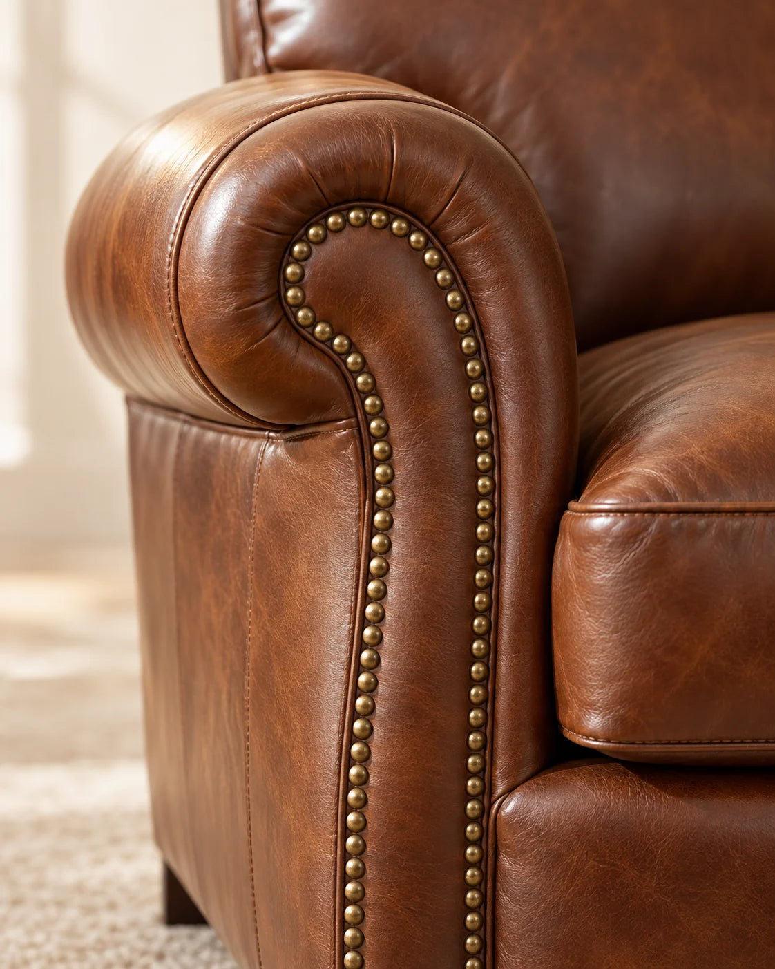Illustrative close-up of antique brass nailhead trim tracing the curved arm of a cognac leather chair